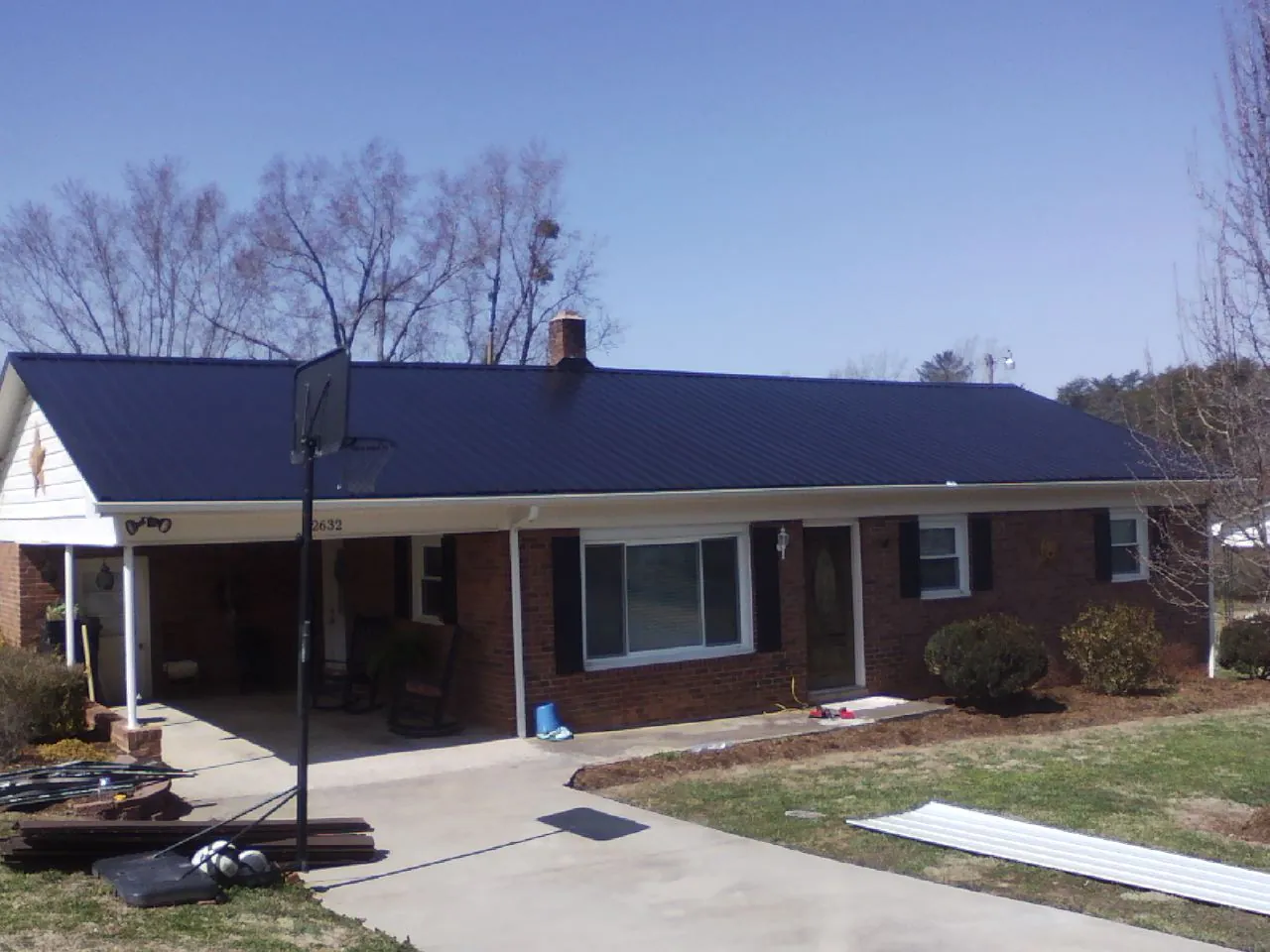 Finished dark blue metal roof on a brick ranch with a carport in Bellefontaine
