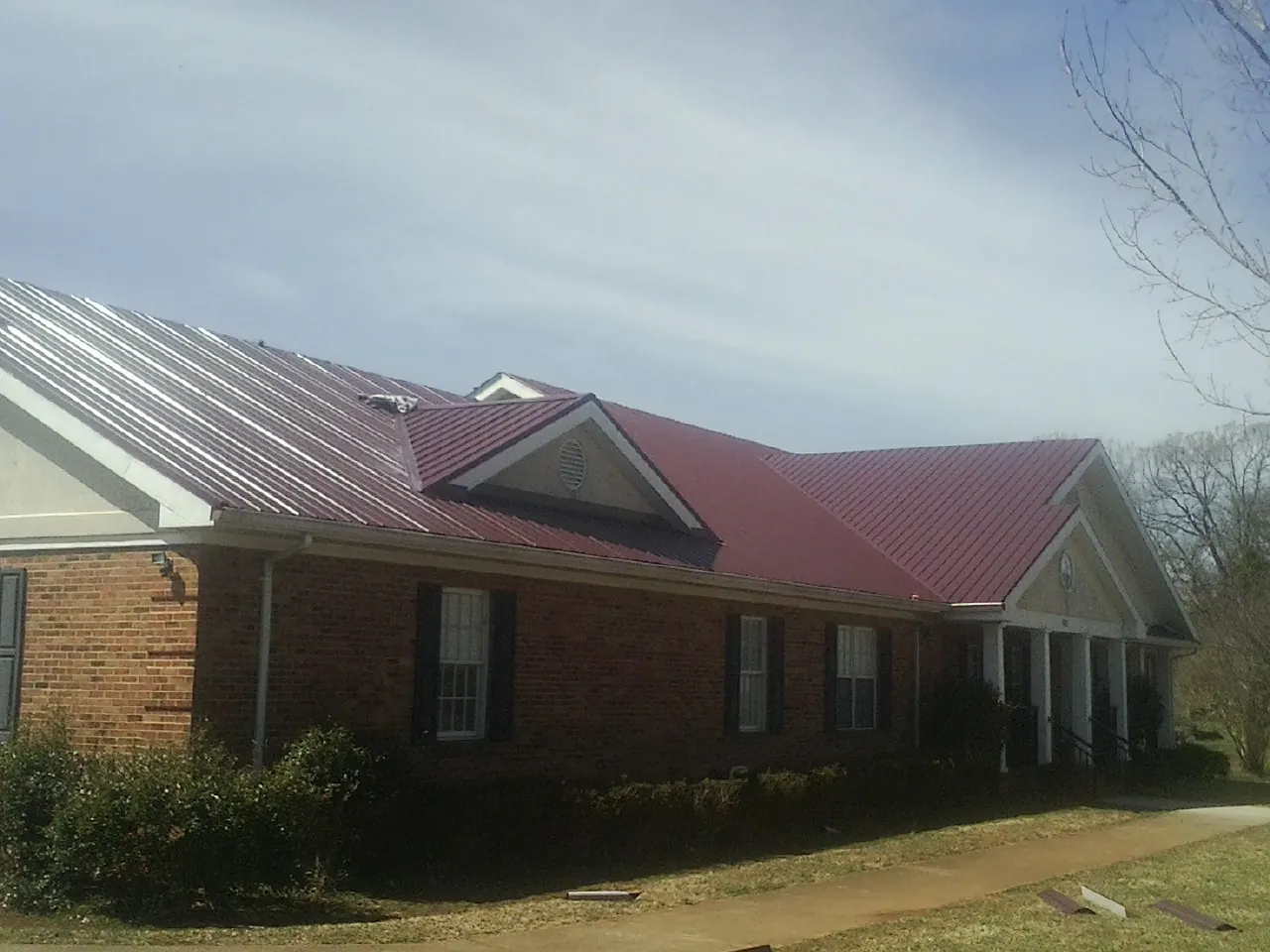 Red metal roof with gabled entries on a long brick building, from a Hail Damage Roof Repair job in Bellefontaine