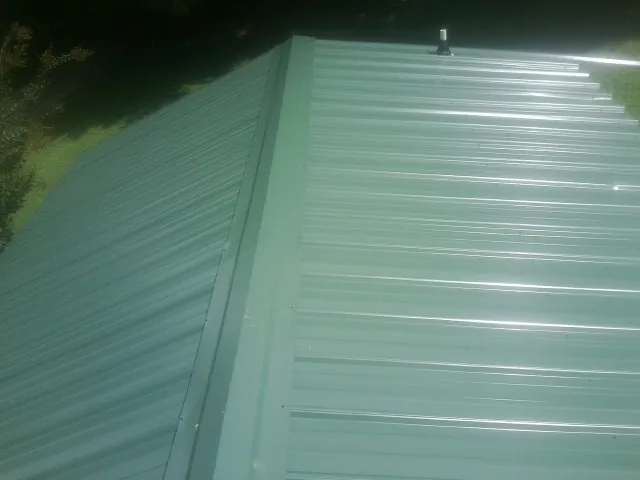 New green metal panels meeting at the ridge of a roof — Flat Roof Repair work by our crew in Bellefontaine
