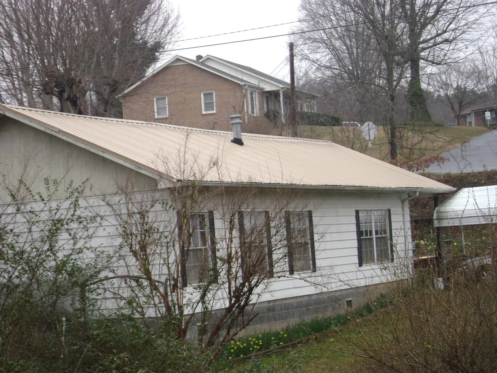 Tan metal roof on a white sided house set into a hillside — Commercial Roofing by Roofing Brothers in Bellefontaine