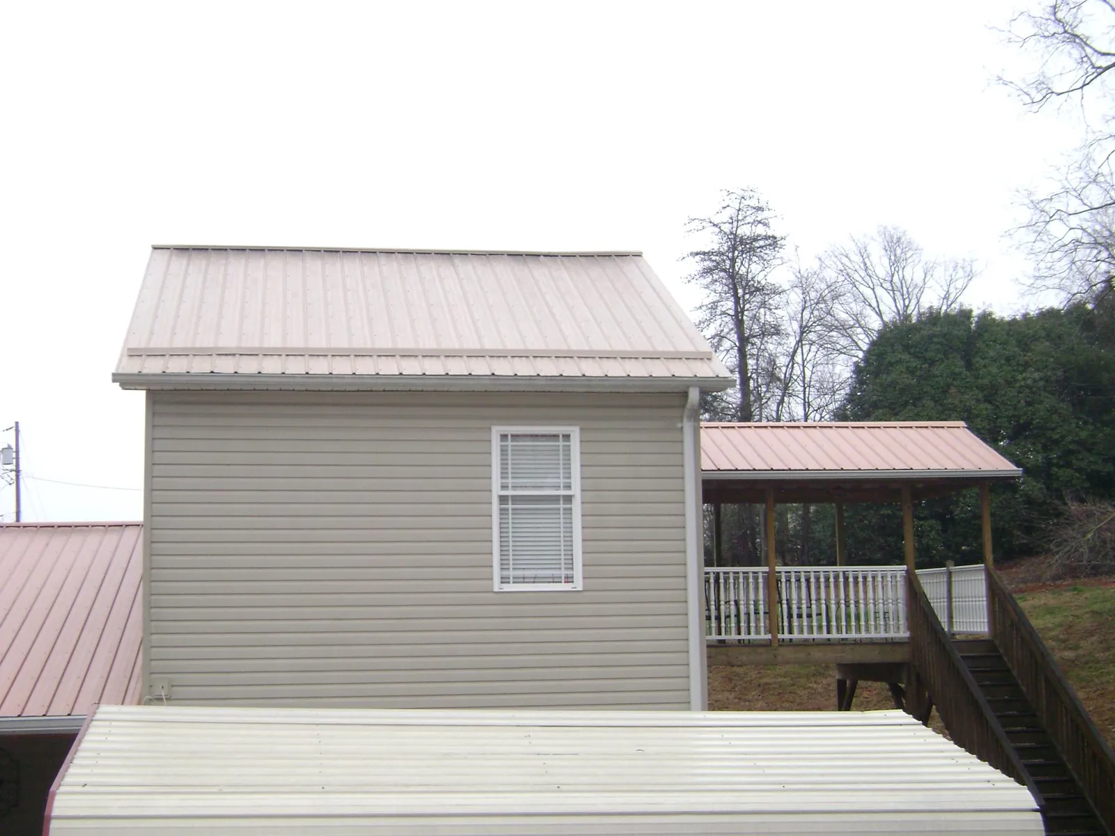 Tan metal roofs on a two story addition and attached porch, from a Roof Replacement job in Bellefontaine